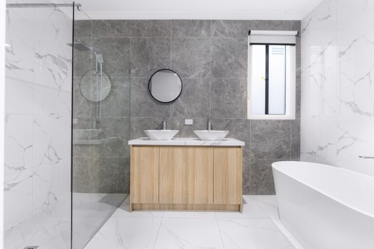 A sleek and stylish modern bathroom with minimalist design, featuring dual washbasins, marble tiles, and a glass shower enclosure.