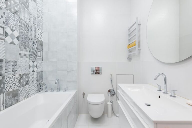Contemporary bathroom featuring white sanitaryware, a round mirror, and patterned wall tiles for a sleek design.