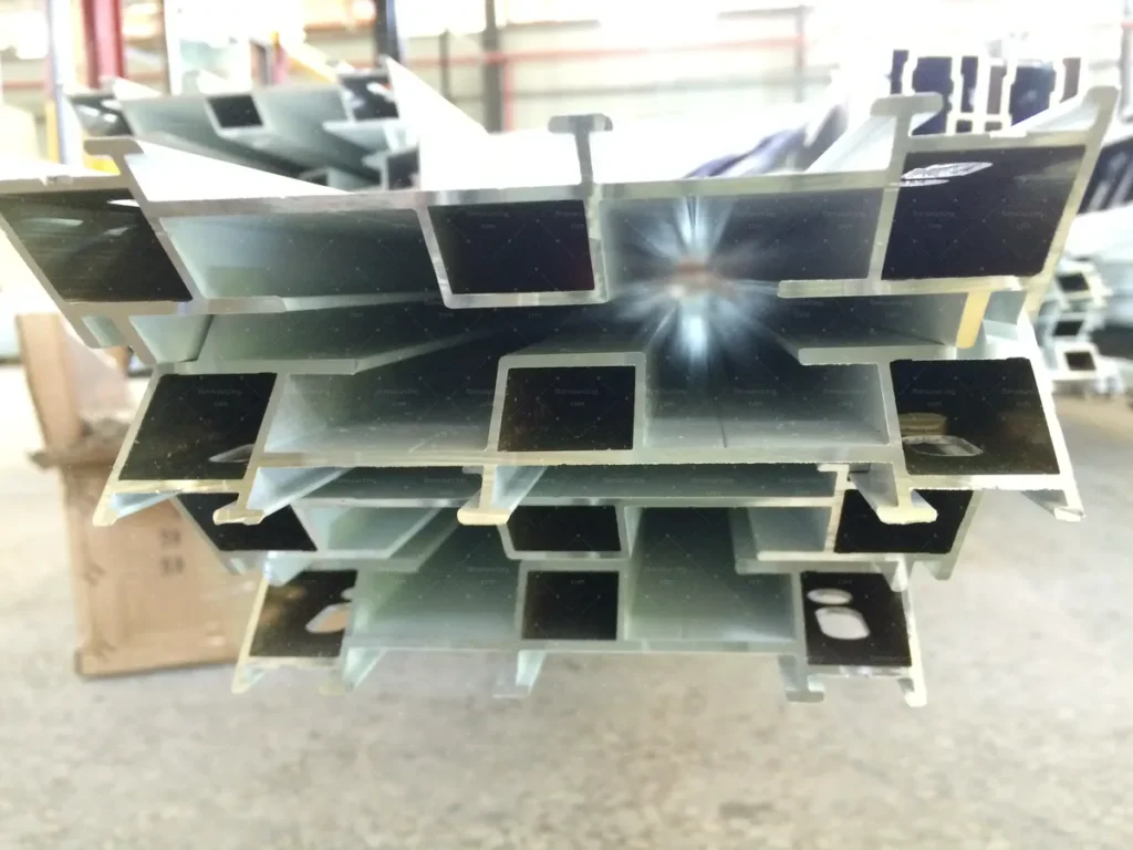 Aluminium window profile cross-sections stacked for inspection at the fabrication factory