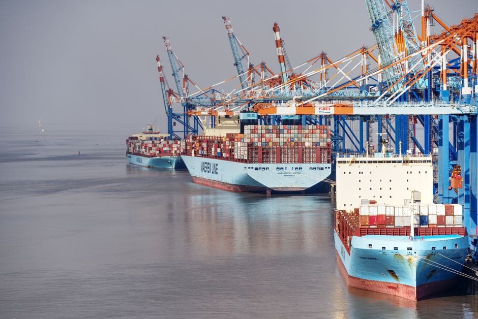 Container ships docked at a busy port with vibrant cranes and clear skies.