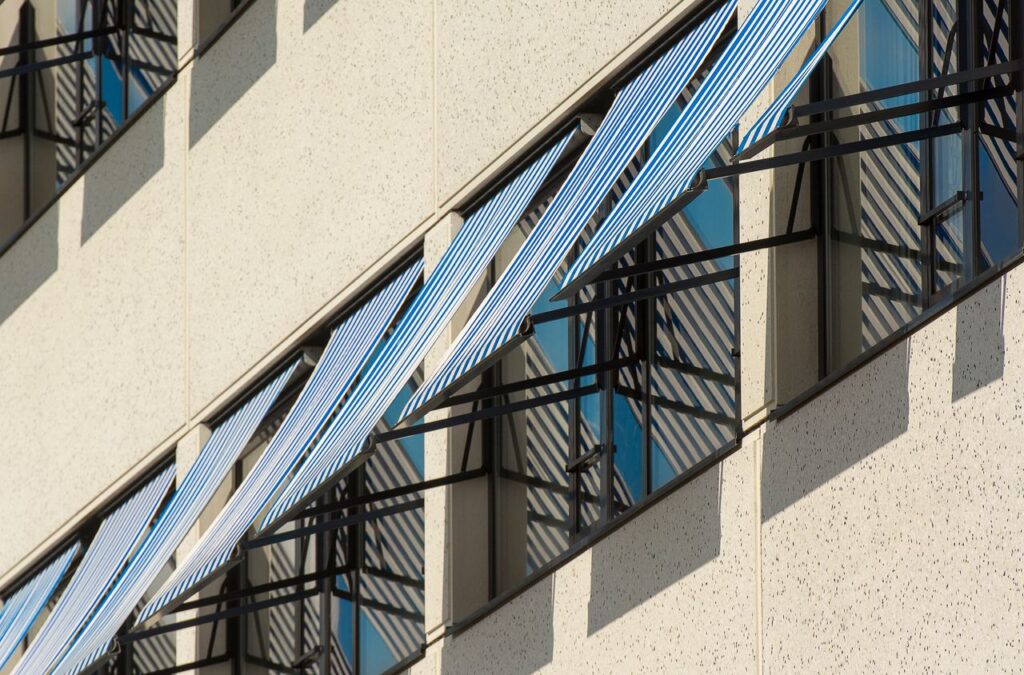Close-up of contemporary building facade with blue and white striped awnings providing shade.