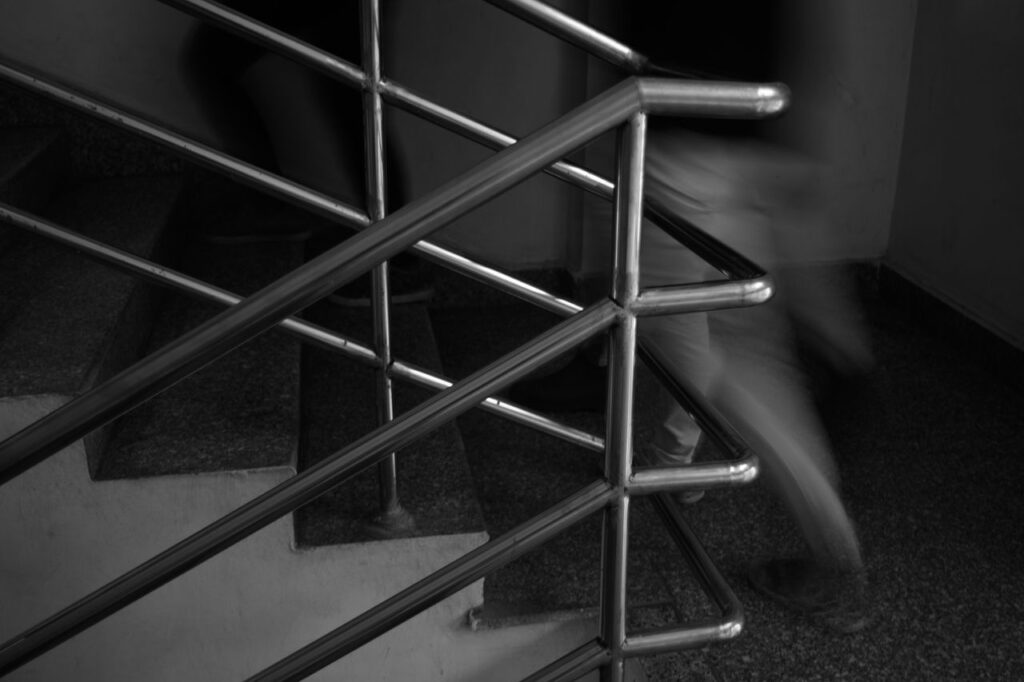 Monochrome image of people moving quickly on stairs with metal railings.