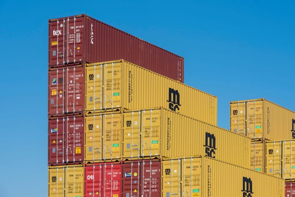 Colorful shipping containers stacked high under a clear blue sky, displaying industrial logistics.