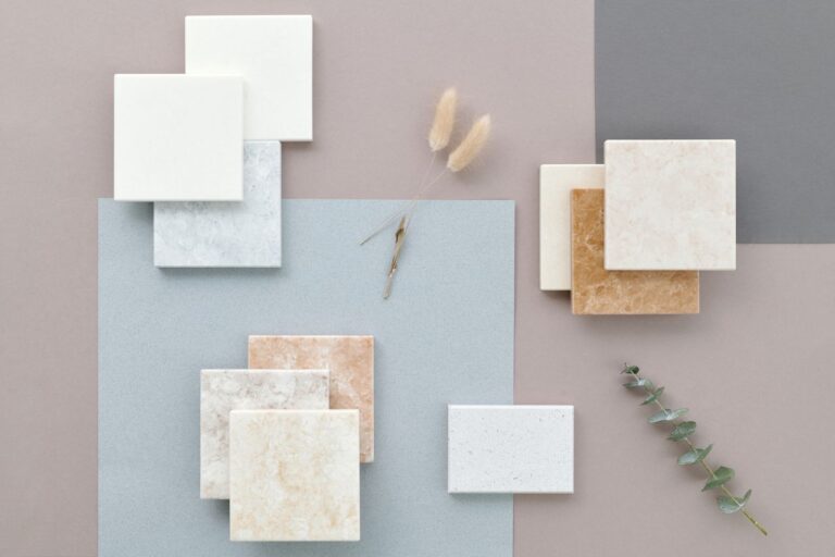 Artistic flat lay of marble and ceramic tiles on a gray surface with subtle plants for interior design inspiration.
