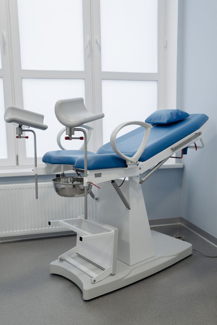 A modern gynecological chair in a sterile medical facility, featuring adjustable armrests and clean design.