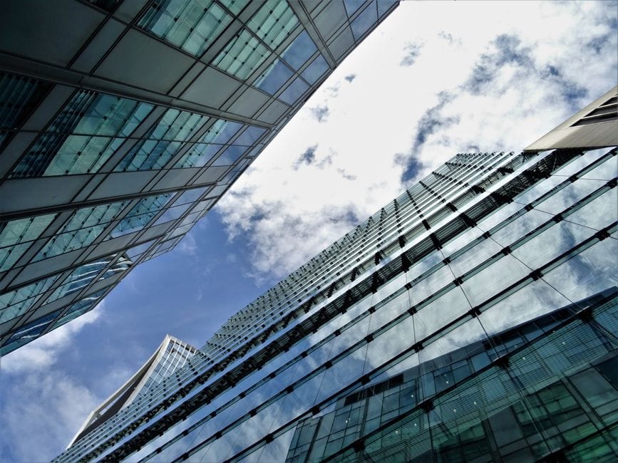 Low-angle view of skyscrapers with reflective glass facades against a blue sky with clouds.