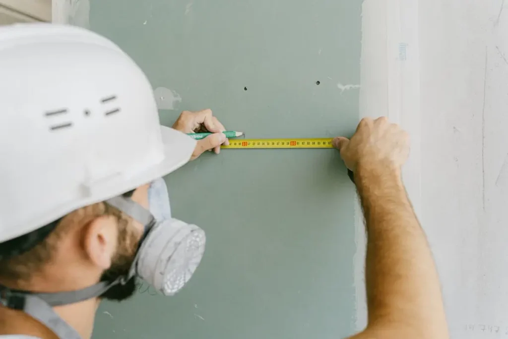 Installer taking an as-built wall dimension — site measurement for custom joinery before China production