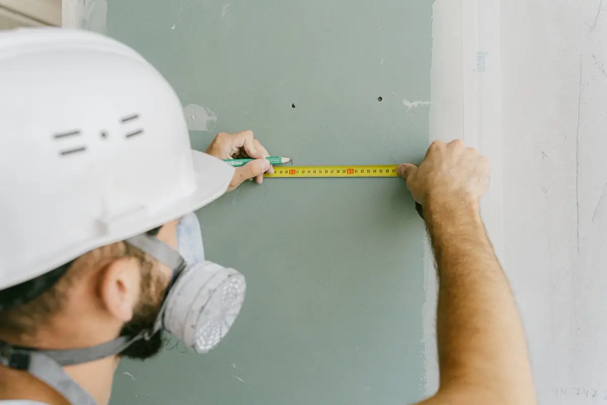 Installer taking an as-built wall dimension — site measurement for custom joinery before China production