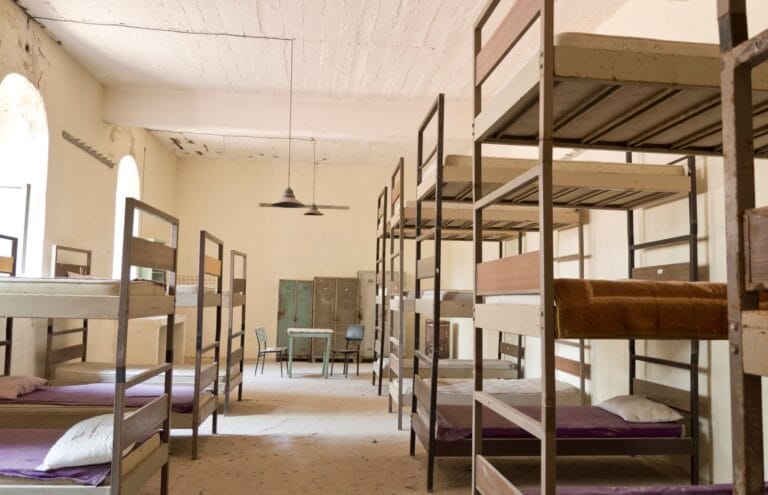 Rows of steel-frame bunk beds with lockers in a shared accommodation dormitory