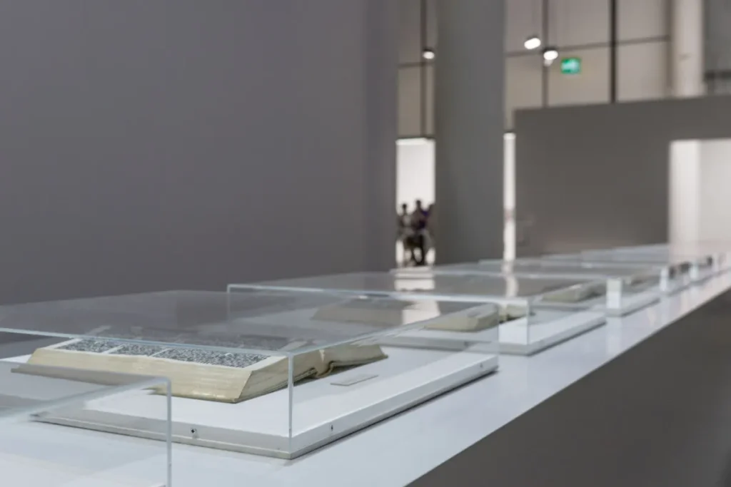 Row of glass museum display cases with open books on a white exhibition plinth