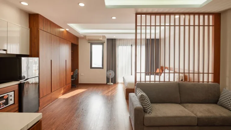 Apartment living area with a brown sofa and a sleeping area behind a timber screen