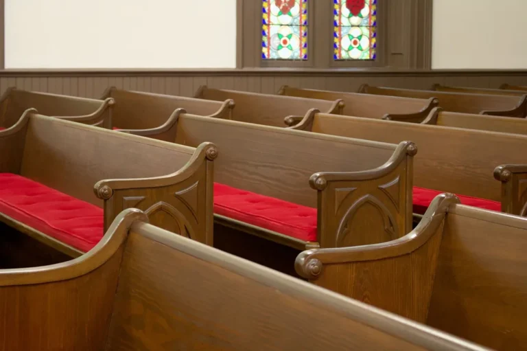 Rows of wooden church pews with red seat cushions