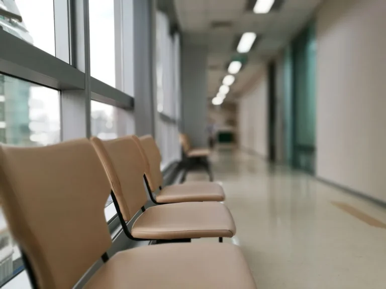 Row of beige waiting chairs along a bright hospital corridor window