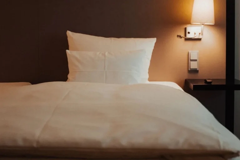 Hotel room with a neatly made bed with white linen and a bedside lamp