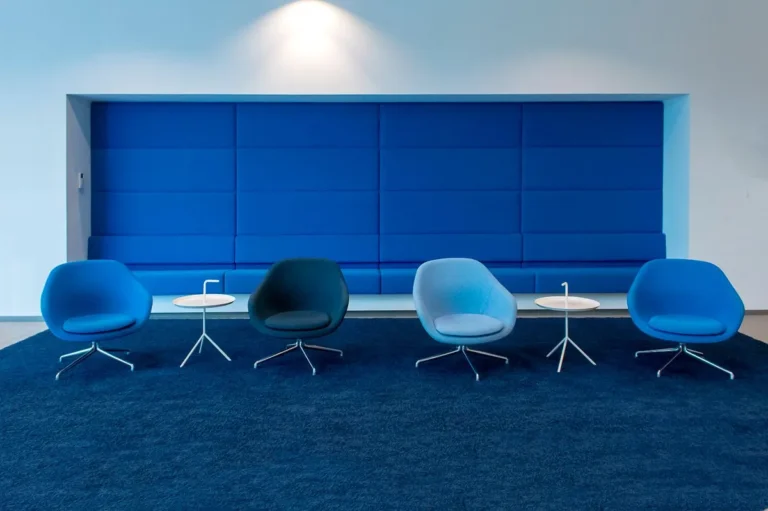 Office lounge with blue shell armchairs and a blue wall-mounted banquette