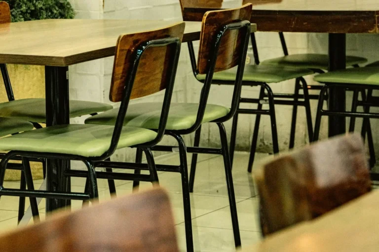 Metal-frame restaurant dining chairs with wooden backs and green seats at timber tables