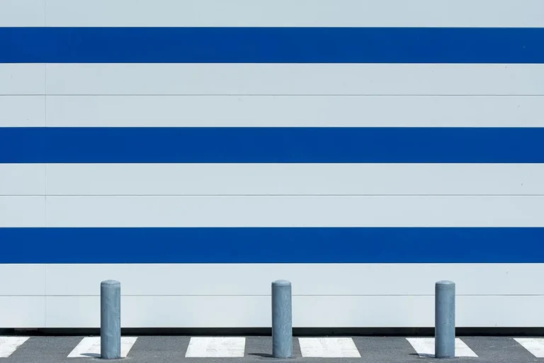 Row of steel bollards beside a white wall with blue stripes