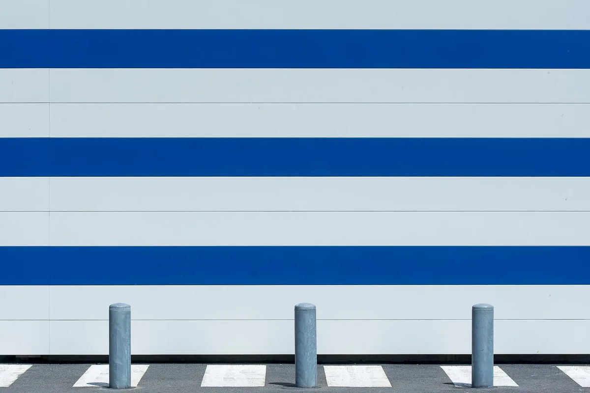 Row of steel bollards beside a white wall with blue stripes