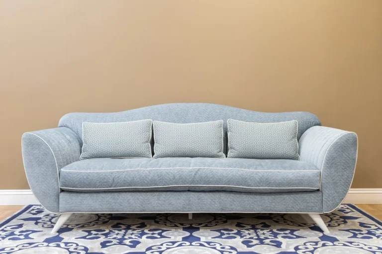 Light blue fabric upholstered sofa with three seat cushions against a beige wall