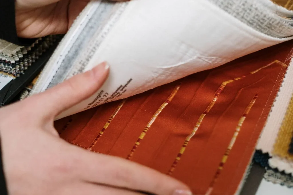 Hands turning pages of a sample book with upholstery fabric swatches