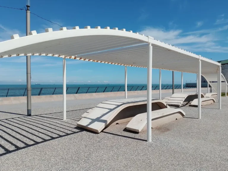 White curved pergola over sun loungers on a seafront under a blue sky