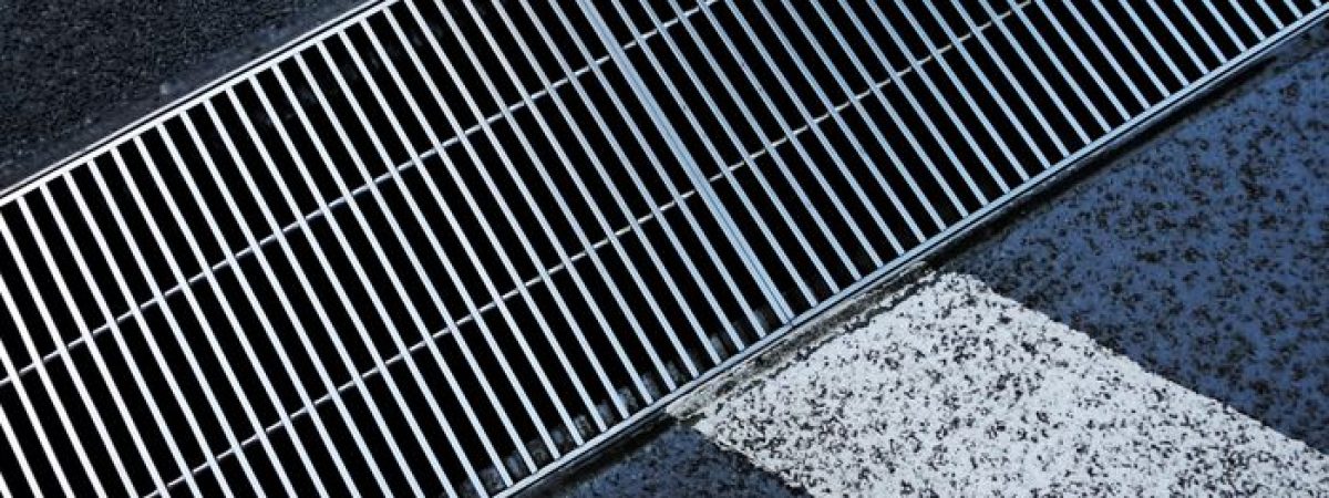 Metallic street grate intersecting white road markings on a textured asphalt surface.