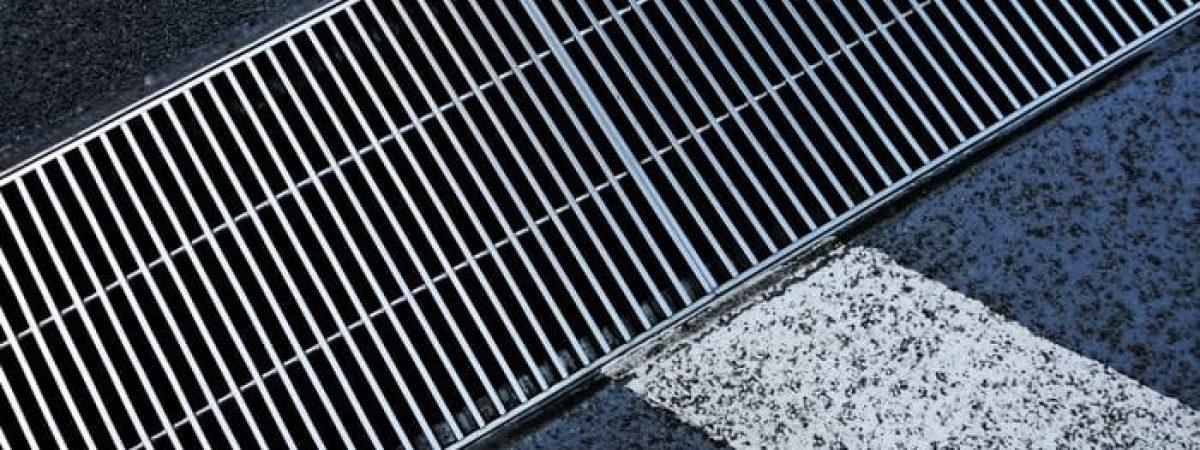 Metallic street grate intersecting white road markings on a textured asphalt surface.