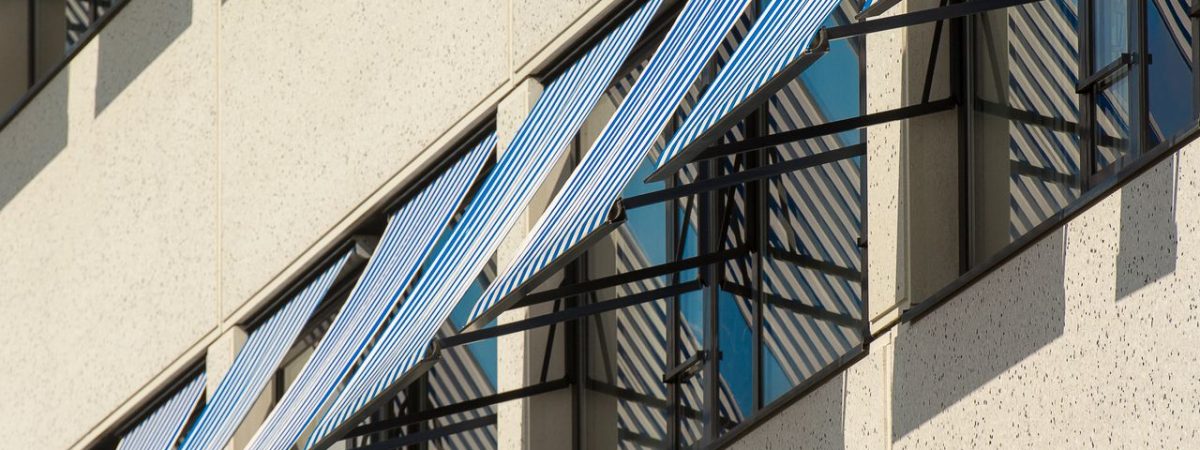 Close-up of contemporary building facade with blue and white striped awnings providing shade.