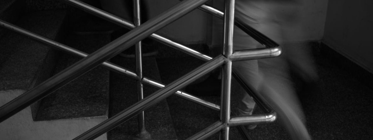 Monochrome image of people moving quickly on stairs with metal railings.