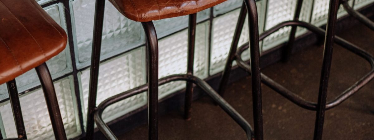 A row of modern bar stools featuring brown leather seats against a glass wall in an indoor setting.